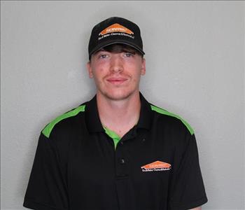 Male employee in hat smiling in front of a grey background.