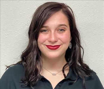 Female employee in black shirt standing in front of a gray background.