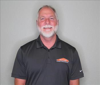 Male employee with grey hair smiling in front of a grey background.