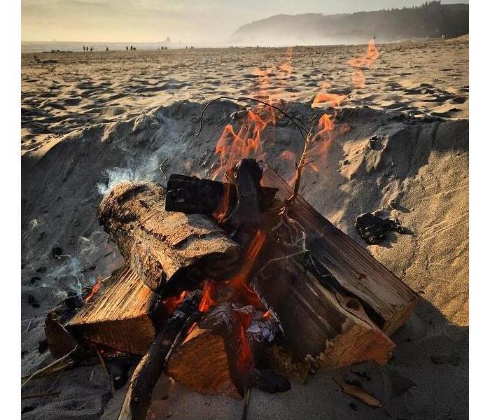 A pile of wood in a hole on a beach on fire. 