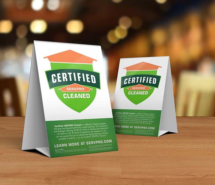 Table tent signs describing the Certified: SERVPRO Cleaned program on top of a wooden table.